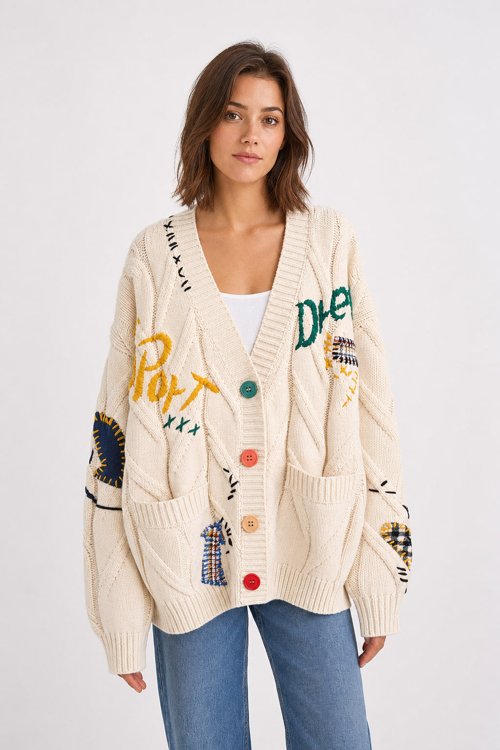 Cardigan oversize écru en maille torsadée vu de face, broderies lettres et boutons colorés dépareillés