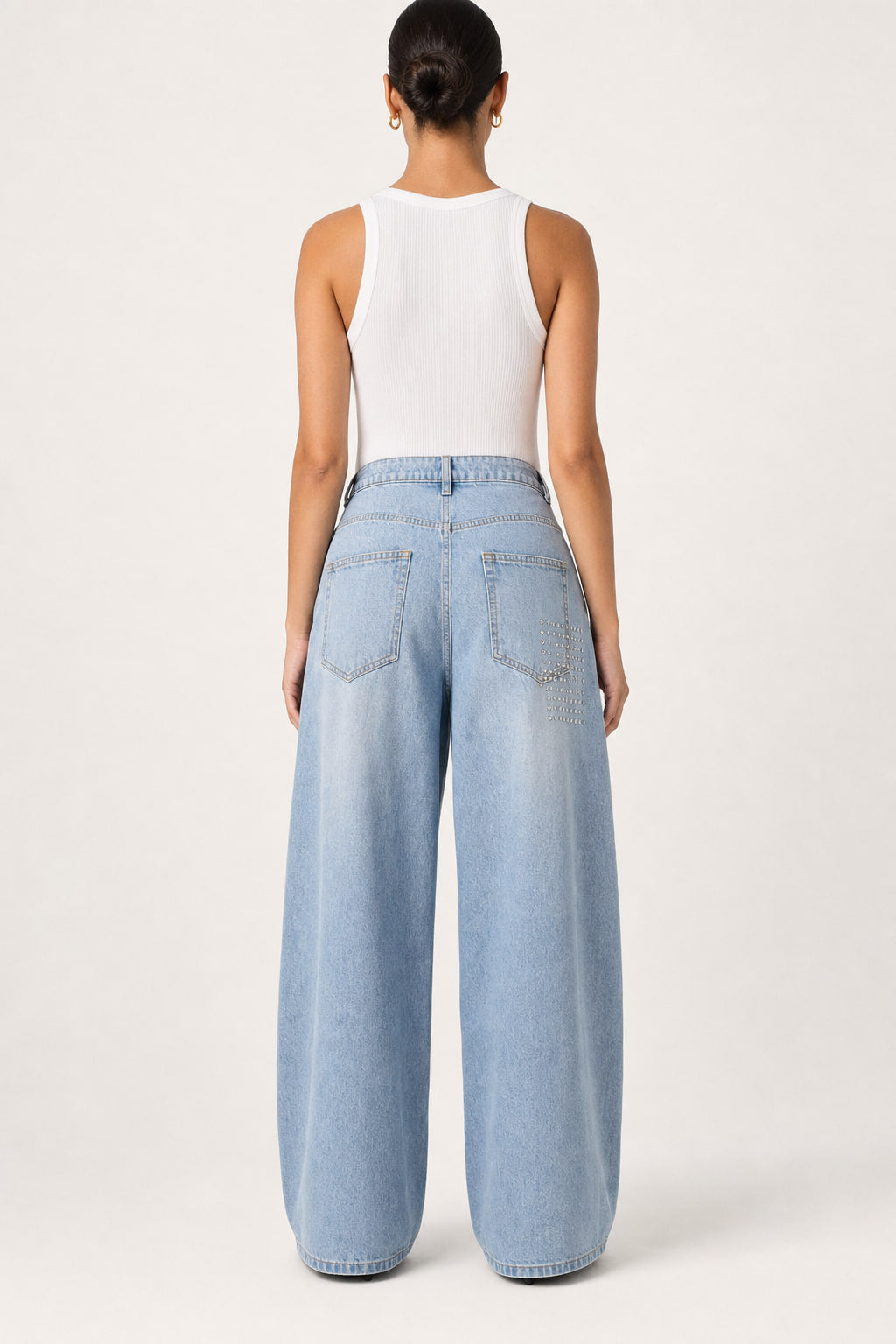 Dos du jean baggy en denim clair, poches plaquées surpiquées dont une ornée de clous