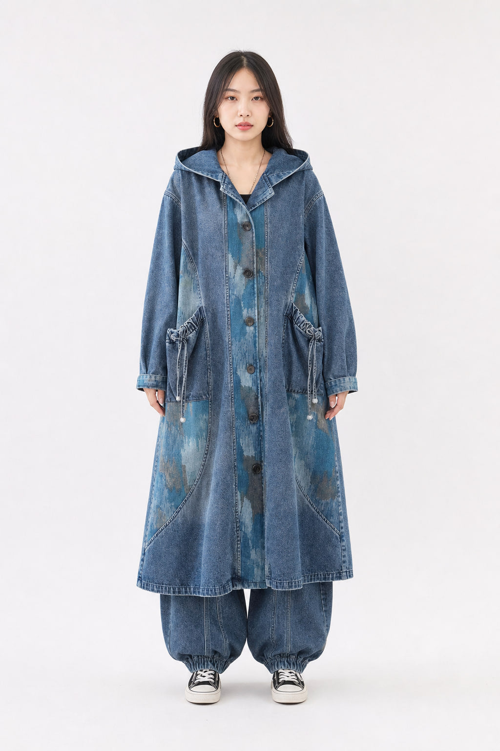 Femme portant un long manteau en jean délavé bleu et kaki à capuche, coupe oversize évasée jusqu'au mi-mollet, vu de face