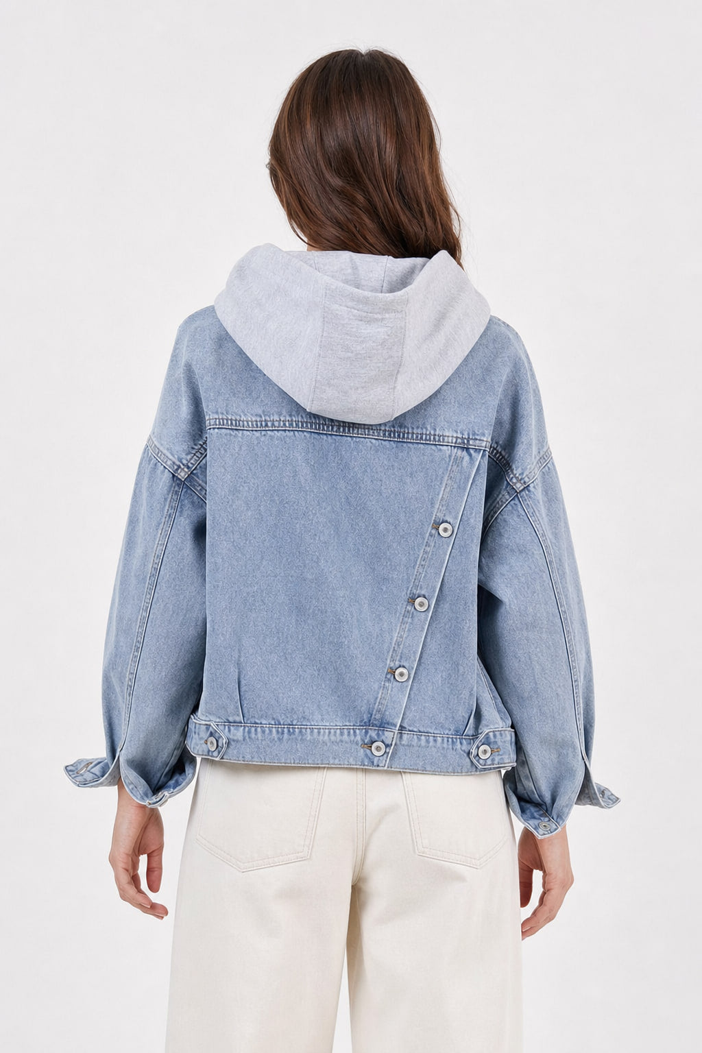 Dos de la veste en jean bleu clair avec sa rangée de boutons en biais et sa capuche grise