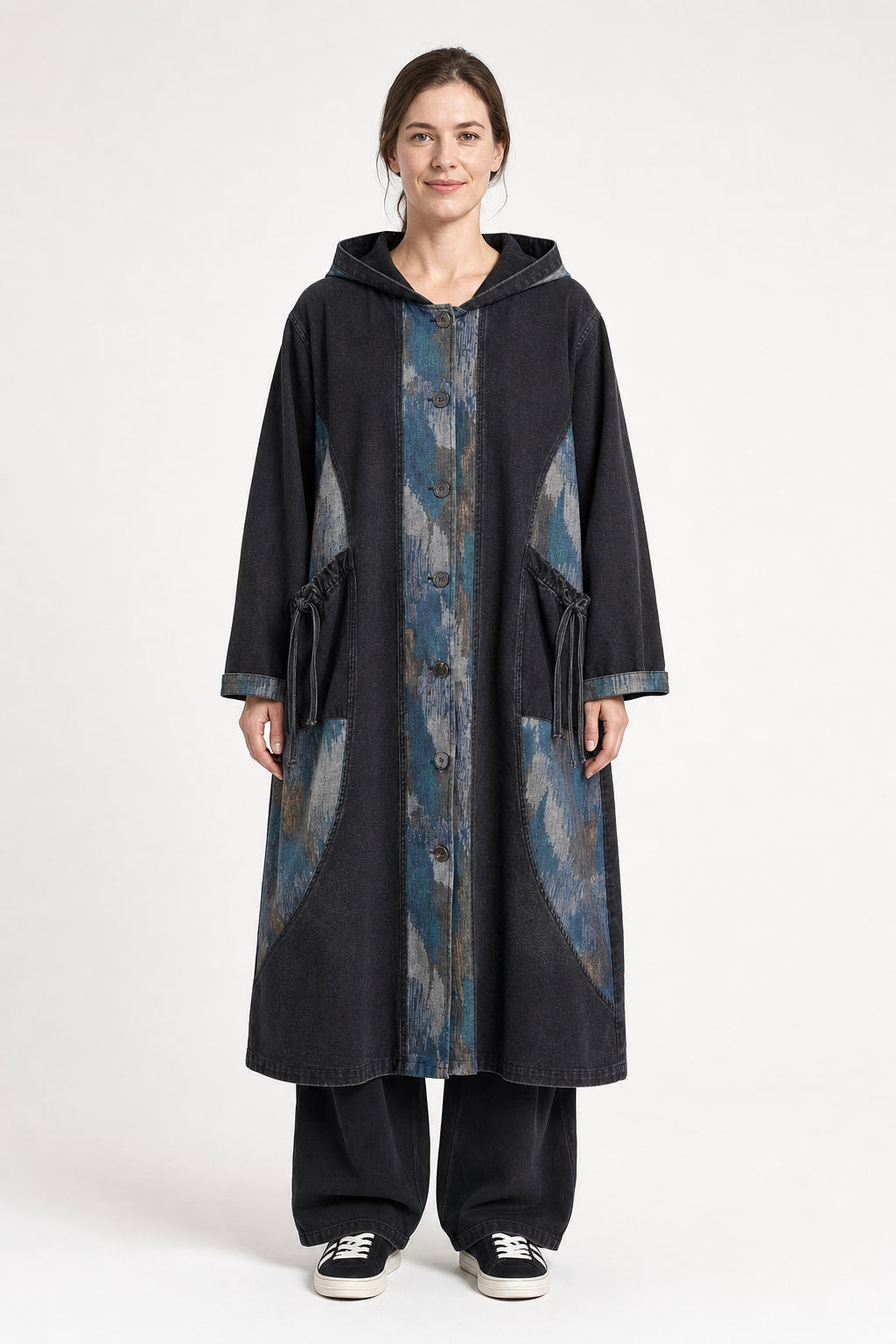 Manteau long en denim à capuche porté ouvert, coupe oversize mi-mollet avec empiècements imprimés bleu, beige et gris sur le devant et grandes poches à rabat