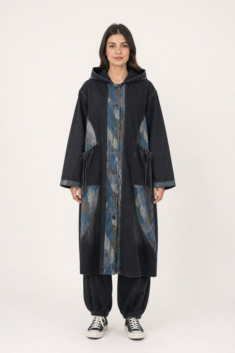Manteau long en denim noir délavé porté de face, capuche rabattue et empiècements imprimés sur le devant