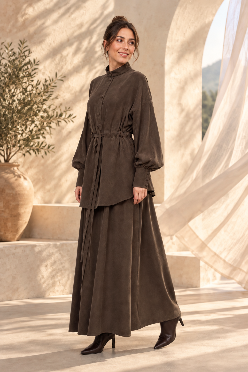 Ensemble tunique boutonnée et jupe longue marron, porté devant un mur de pierre clair — décor généré par IA, vêtement inchangé