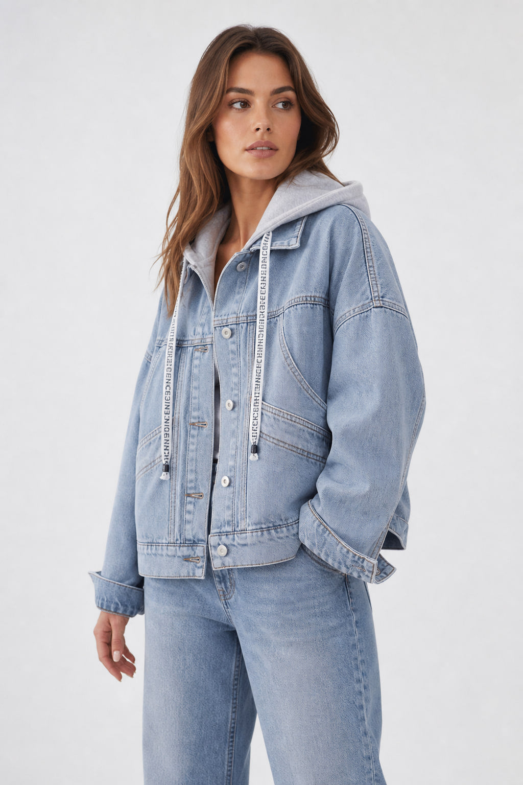 Veste en jean bleu clair vue de trois quarts gauche, bande de taille boutonnée et capuche grise à cordons imprimés